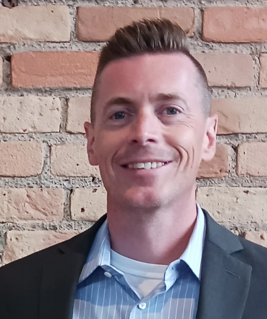 Dan Moen posing by a brick wall smiling